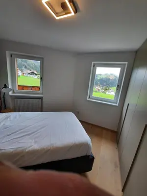 a bedroom with a bed and two windows at Luxury Apartment Daema in Selva di Val Gardena