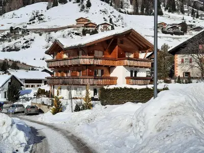a large wooden house in the snow with cars parked at Luxury Apartment Daema in Selva di Val Gardena