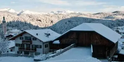 a building covered in snow with mountains in the background at Wegmacherhof in Castelrotto