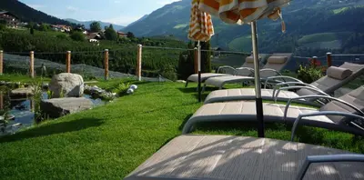 a row of benches with an umbrella on the grass at Ferienwohnungen Braiter in Rifiano