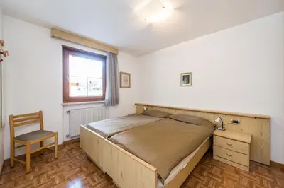 a bedroom with a bed and a chair and a window at Appartamenti Cèsa Crepa Neigra in Canazei