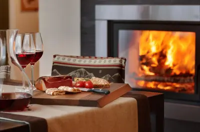 a table with a glass of wine and a fireplace at Crioli Dolomiti Lodge in Villabassa