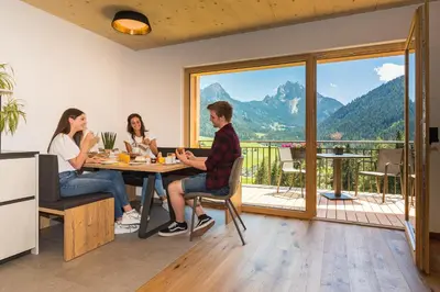 three people sitting at a table with a view of a mountain at Residence Bergheim in Braies