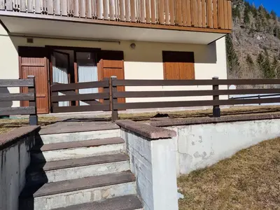 a house with wooden doors and stairs in front of it at Appartamento con giardino in Predazzo