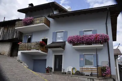 a white house with purple flowers on balconies at Casa Tania in Pozza di Fassa