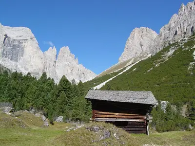 a log cabin on a hill with mountains in the background at Casa Tania in Pozza di Fassa