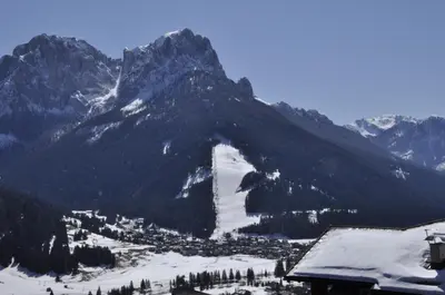 a snow covered mountain with a town in front of it at Casa Tania in Pozza di Fassa