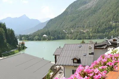 a view of a lake and mountains with pink flowers at Hotel Coldai in Alleghe