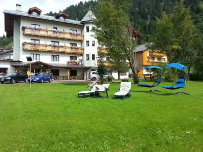 a green yard with chairs and a hotel at Hotel Edelweiss in Val di Zoldo