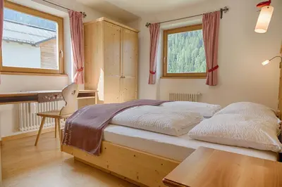 a bedroom with a bed and a desk and two windows at Cademia in Ortisei