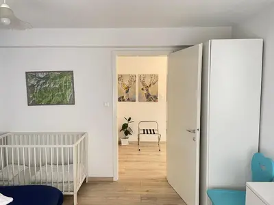a white nursery with a crib and a chair in a room at SUITE DOLOMITI Appartamento in Falcade