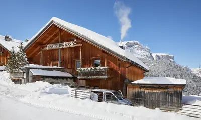 a log cabin in the snow with smoke coming out at Pension Angelo in Corvara in Badia