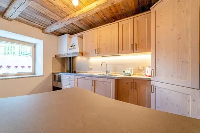 a kitchen with wooden cabinets and a sink and a window at Ospitalità Diffusa Laste Dolomites Cèsa del Bèrba Jaco in Rocca Pietore