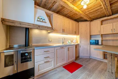 a kitchen with white cabinets and a wooden ceiling at Ospitalità Diffusa Laste Dolomites Cèsa del Bèrba Jaco in Rocca Pietore