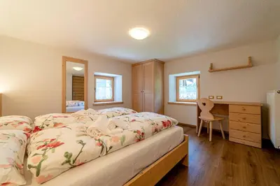 a bedroom with a large bed and a desk at Ospitalità Diffusa Laste Dolomites Cèsa del Bèrba Jaco in Rocca Pietore