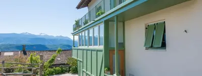 a green and white building with a window and mountains at Haus Pobitzer in Caldaro