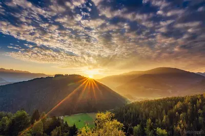 a sunset in the mountains with the sun setting on a hill at Kehrerhof Urlaub auf dem Bauernhof in San Lorenzo di Sebato