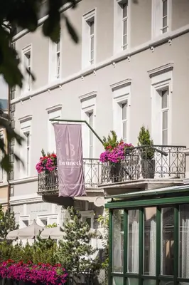 a building with two balconies with flowers and a flag at Hotel Bruneck Design-Suites in Brunico