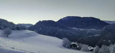 a house on a snowy hill with mountains in the background at Alpine Chalet Aurora Dolomites in Laion