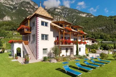 a building with chairs in a yard with mountains in the background at Santlhof - Sauvignon in Cortaccia