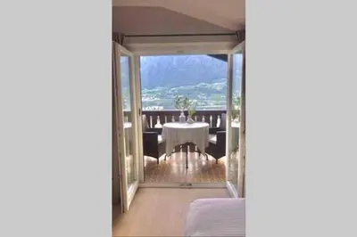 a room with a table and a balcony with a view at Villa Corazza-Bezauberndes Appartment+ Schwimmbad in Tirolo