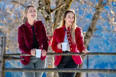two girls are holding coffee cups on a fence at Hotel Leonhard in Nova Ponente