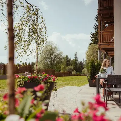 a woman sitting at a table in a garden at Hotel Leonhard in Nova Ponente