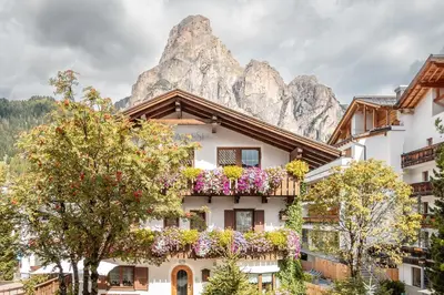 a building with flowers in front of a mountain at Villa Resi B&B in Corvara in Badia