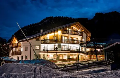 a building with lights on in the snow at night at Hotel Garni Aghel in Selva di Val Gardena