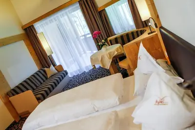 a room with two beds and a couch and a window at Hotel Garni Aghel in Selva di Val Gardena