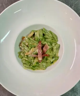 a white plate with a dish of green pasta with bacon at Hotel Villa Aurora in San Martino di Castrozza