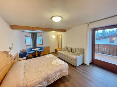 a bedroom with a bed and a couch and a window at Hotel Villa Aurora in San Martino di Castrozza
