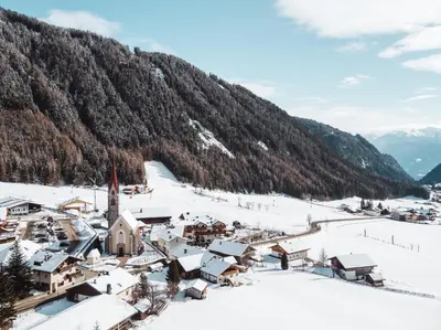 a village covered in snow with a mountain in the background at Familienhotel Huber in Valles