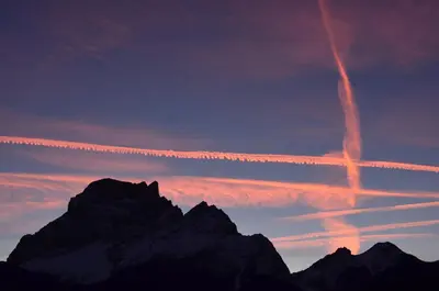 a sunset over the mountains with a plane trail in the sky at Residence Peniè in San Vito di Cadore
