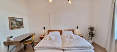 a bedroom with a bed with white sheets and a desk at Rosa Rooms Meran in Merano