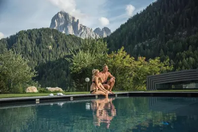 a man and a woman sitting on the edge of a swimming pool at Apartments Diamant in Ortisei