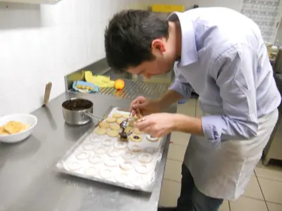 a man standing in a kitchen preparing a cake at Albergo Alpino in Arabba