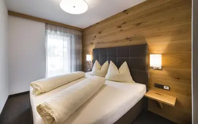 a bedroom with a large white bed with a wooden wall at mittendorf klimaresidence in Schenna
