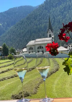 two glasses of white wine on a table with a church at La Ücia by Fana Ladina in San Vigilio Di Marebbe