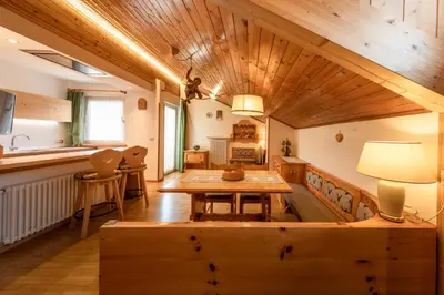 a dining room with a wooden table and a kitchen at Majon d'Aisciuda in Vigo di Fassa