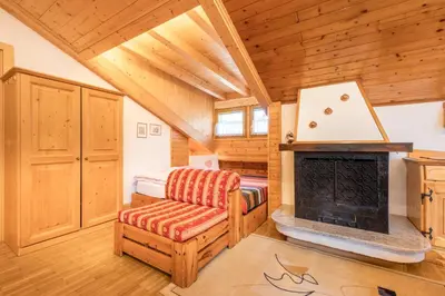 a log cabin bedroom with a fireplace and a chair at Majon d'Aisciuda in Vigo di Fassa