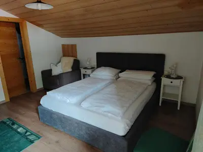 a bedroom with a large bed and a chair at Garni Hattlerhof B&B in Brunico