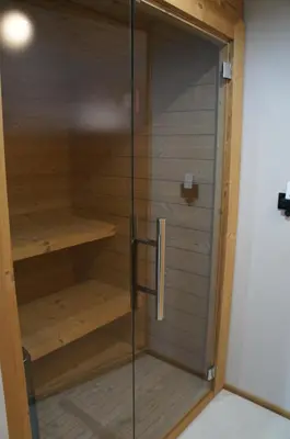 a sauna with a glass door and wooden shelves at Apartment Al Sasso in Taibon
