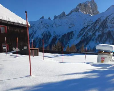a snow covered field with a building and mountains at Casa Neve e Sole - presso Sussy Residence in Falcade