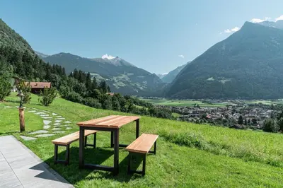 a picnic table and two benches on a hill with a view at Innermoser Bauernhof - Chalets in Molini di Tures