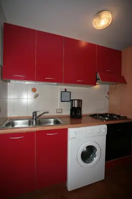 a kitchen with red cabinets and a sink and a washing machine at Appartamenti Cercenà in Canazei