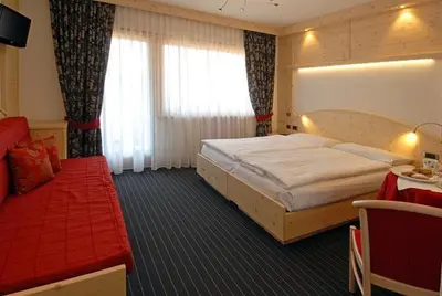 a bedroom with a large bed and a red couch at Hotel Flora Alpina in Campitello di Fassa