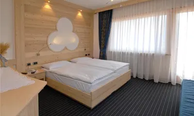 a bedroom with a bed and a large window at Hotel Flora Alpina in Campitello di Fassa