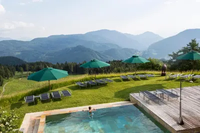 a swimming pool with chairs and umbrellas and mountains at Berghütte Sommerstall in Redagno