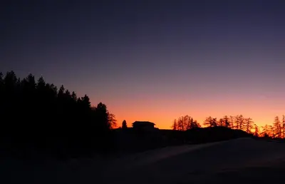 a sunset in the mountains with trees in the foreground at Berghütte Sommerstall in Redagno